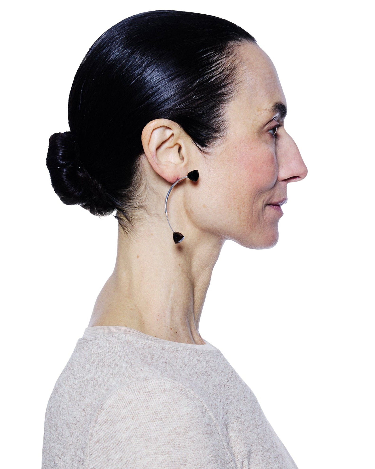Side profile of a person with dark hair pulled back, wearing hoop earrings on a white background